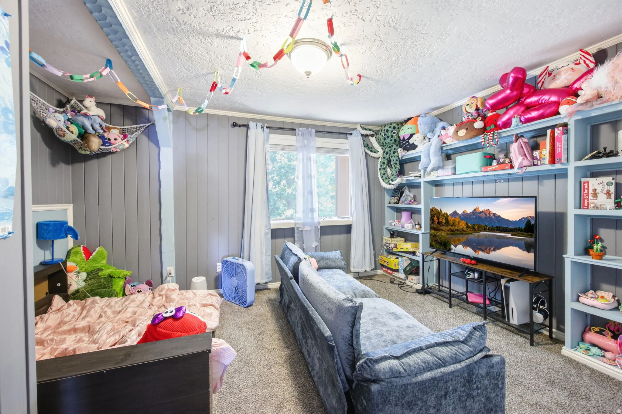 Carpeted interior space featuring a window, textured ceiling, vertical paneling on walls, and built-in shelving