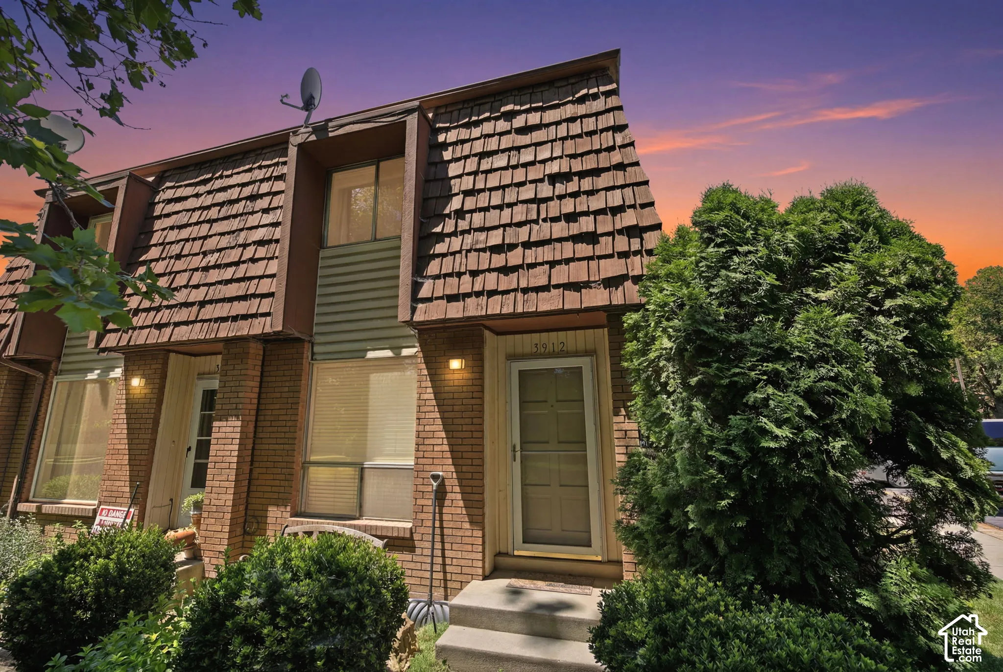 Townhome exterior featuring brick and siding facade, dimensional shingle roof, established evergreen landscaping, and front entry with steps