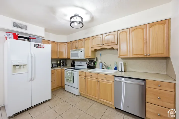 Kitchen featuring light wood cabinetry, light-toned countertops, ceramic tile flooring, a white drop-in sink, and a stainless steel dishwasher