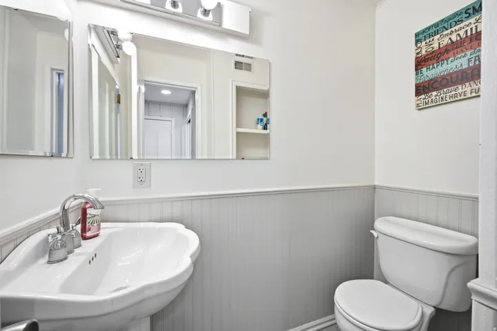 Bathroom featuring a pedestal sink with chrome faucet, a toilet, and beadboard wainscoting