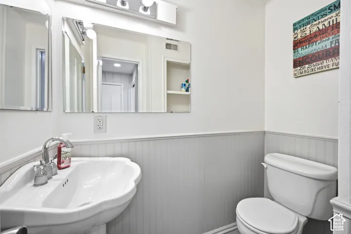 Bathroom featuring a pedestal sink with chrome faucet, a toilet, and beadboard wainscoting