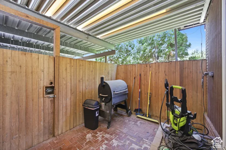 Covered outdoor patio area featuring a corrugated metal roof, brick paver flooring, and natural wood privacy fencing