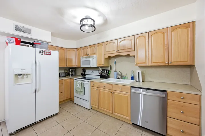 Kitchen featuring light wood cabinetry, light-toned countertops, ceramic tile flooring, a white drop-in sink, and a stainless steel dishwasher