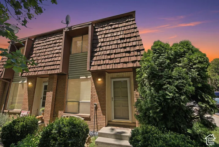 Townhome exterior featuring brick and siding facade, dimensional shingle roof, established evergreen landscaping, and front entry with steps