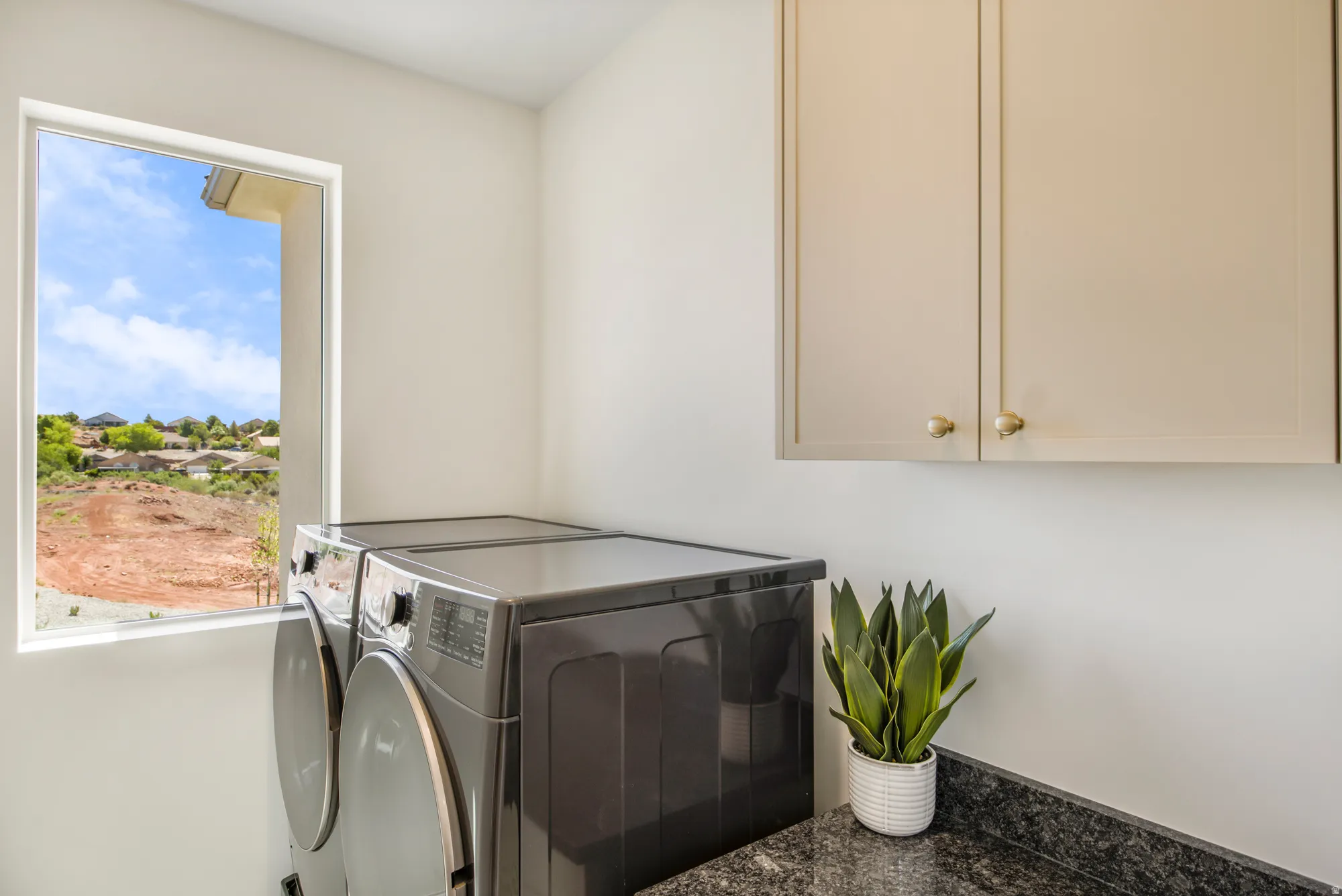 Laundry area featuring a large window, upper cabinetry with gold-tone hardware, and a dark stone countertop