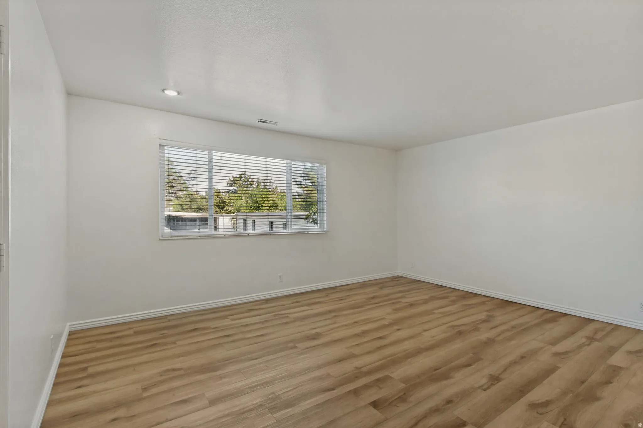 Recessed ceiling lighting, wood-finish flooring, and a large window with blinds