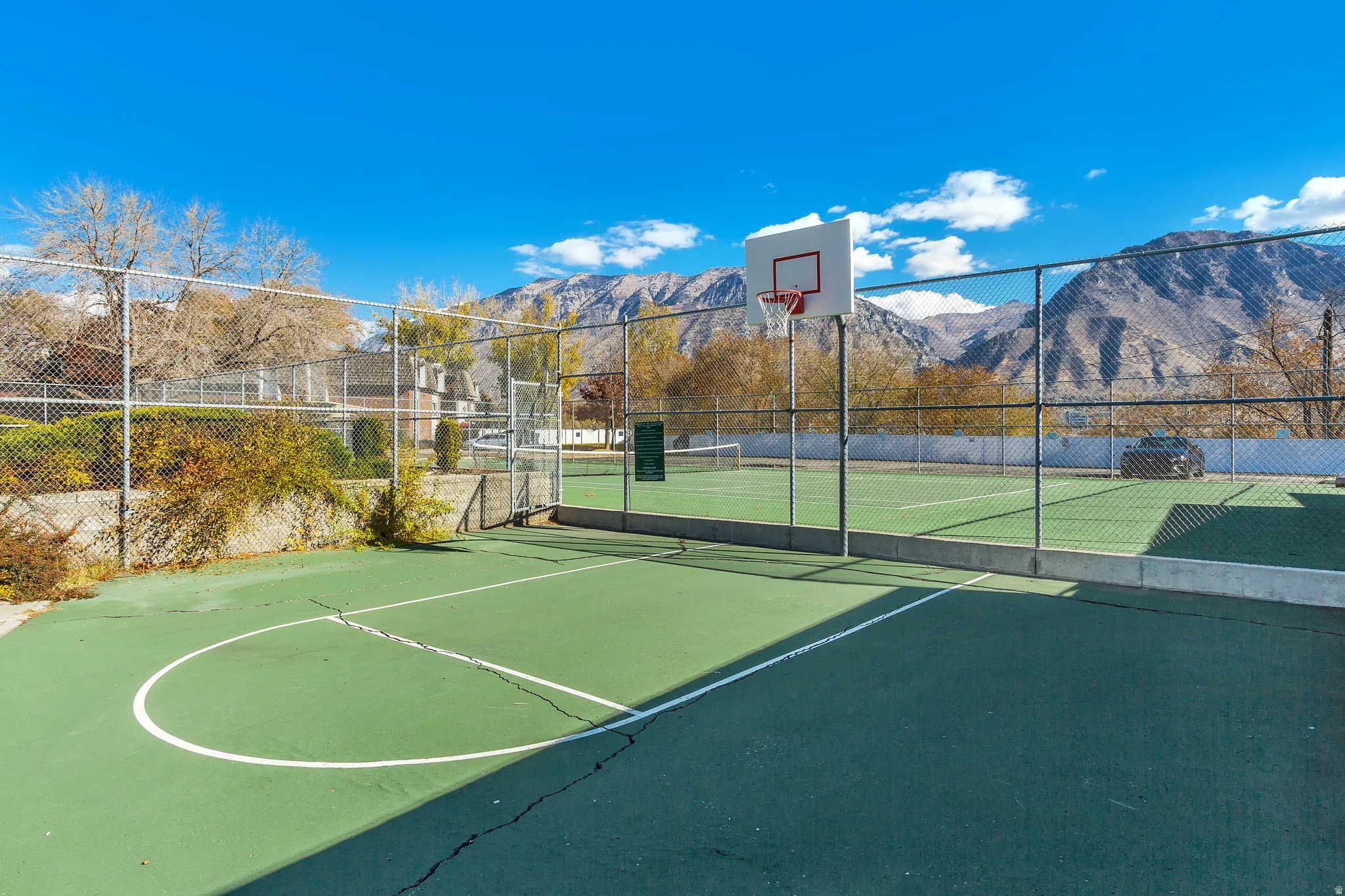 Outdoor court area featuring a basketball hoop and a fenced tennis court