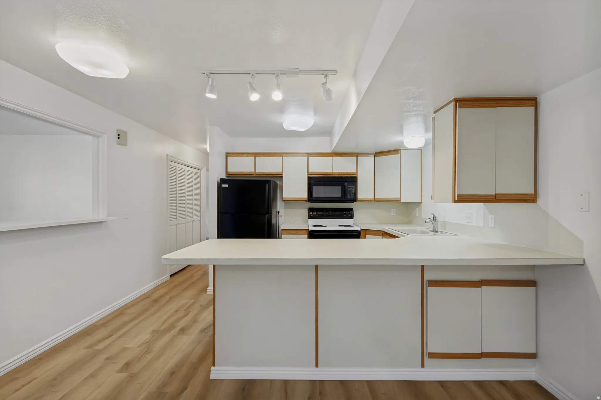 Modern kitchen featuring white cabinetry with wood-finish trim, stainless steel appliances, a waterfall-edge countertop with undermount sink, pendant lighting, and wood-finish flooring throughout the open layout