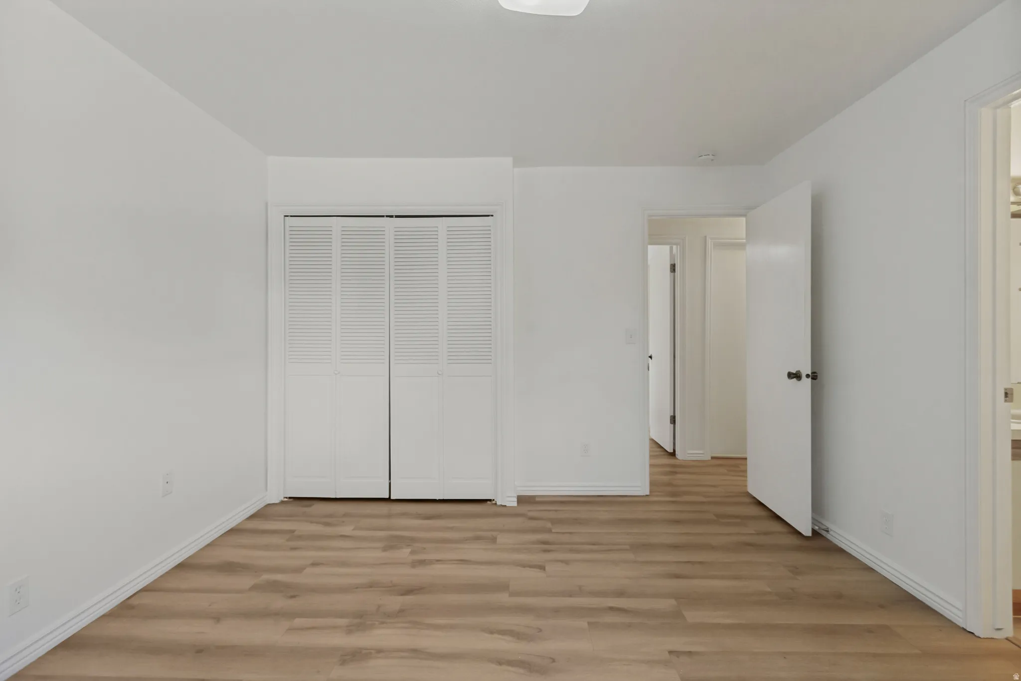 White interior walls, wood-finish flooring, white louvered closet doors, and white interior doors with dark hardware