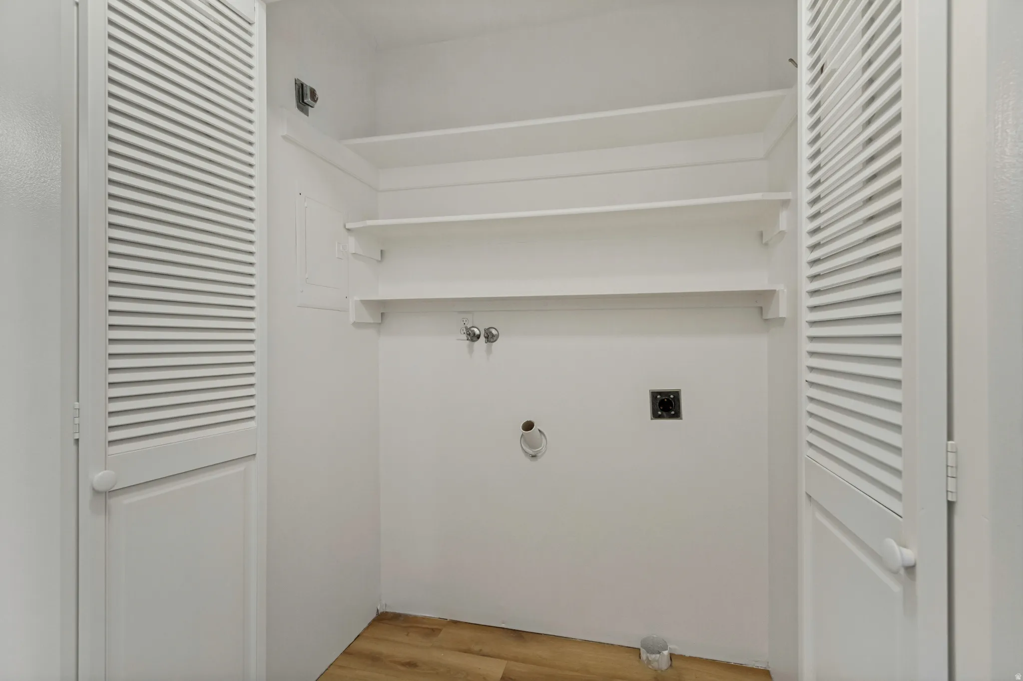 Laundry area with wood-finish flooring, louvered bi-fold doors, and built-in shelving