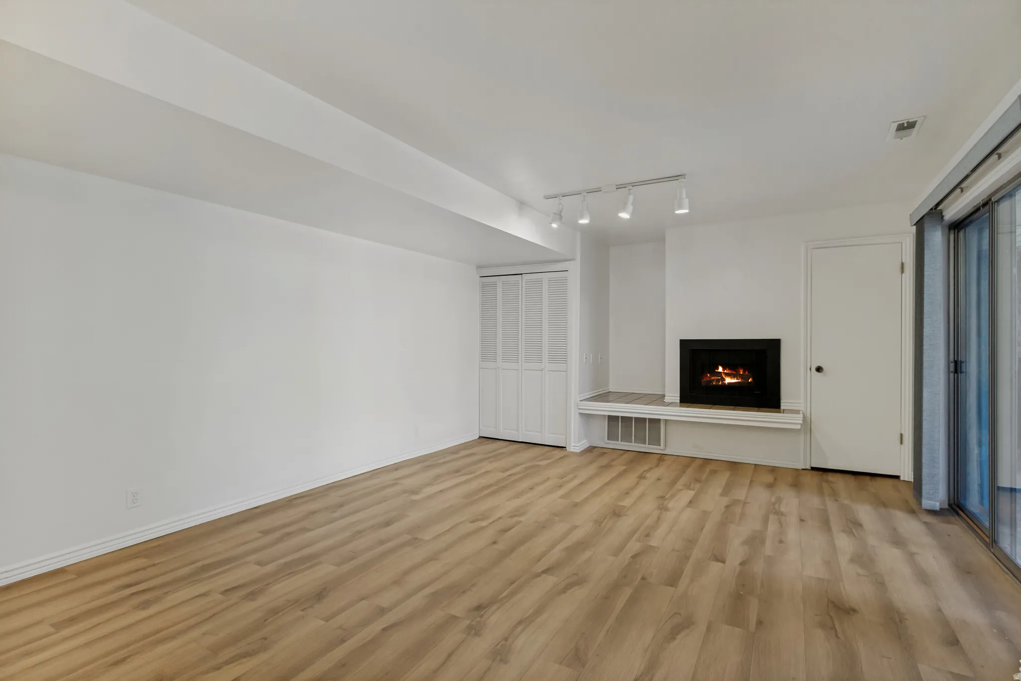 Wood-finish flooring, built-in fireplace with hearth, track lighting, sliding glass door, and bi-fold closet doors