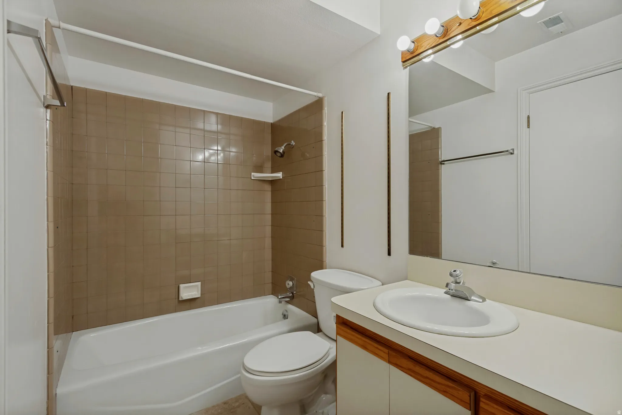 Bathroom featuring a built-in tub with tile surround, a single vanity with an integrated sink, a large wall-mounted mirror, and a wood-finish light fixture