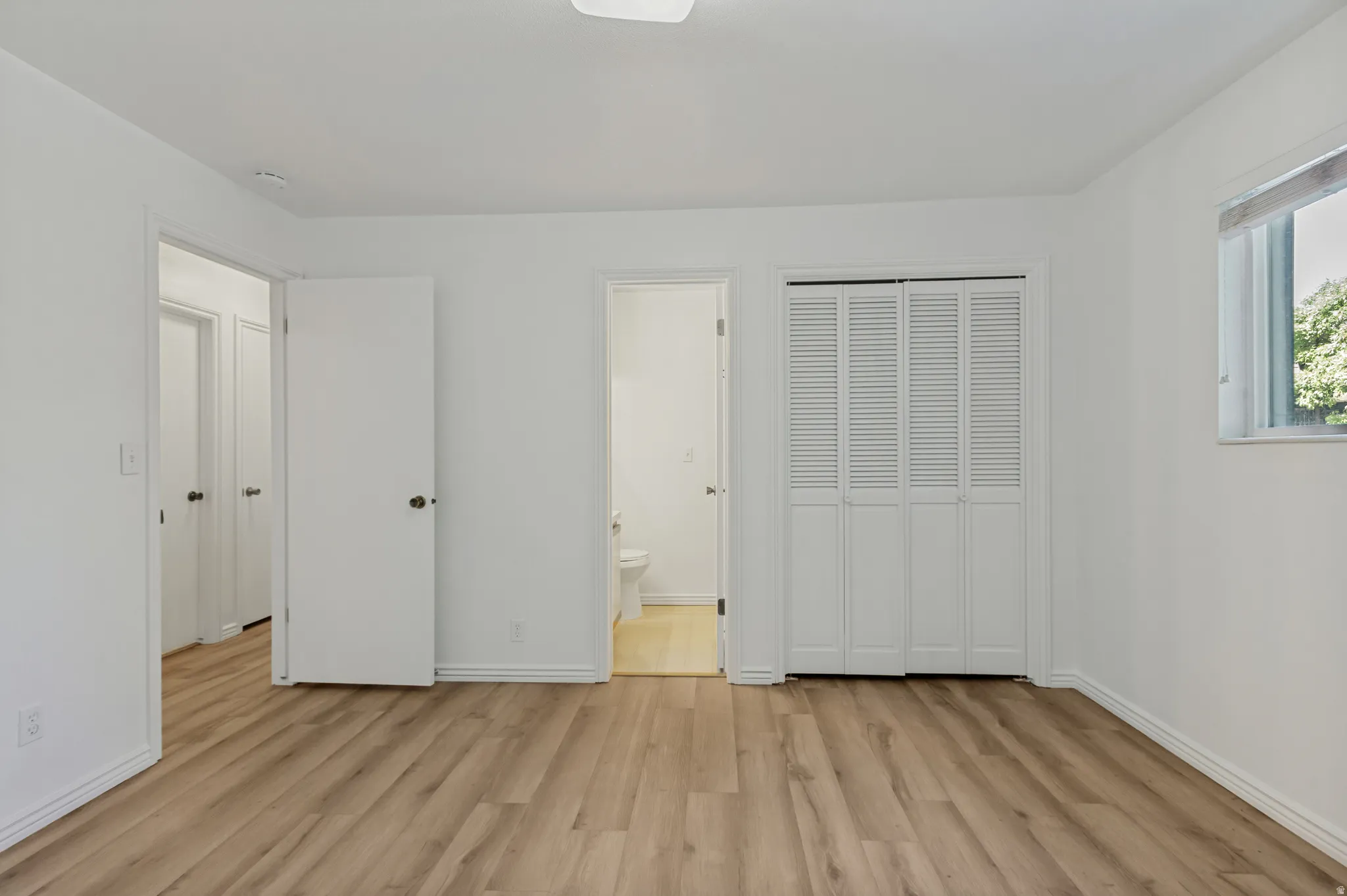 Wood-finish flooring, white walls, louvered bi-fold closet doors, and white trim