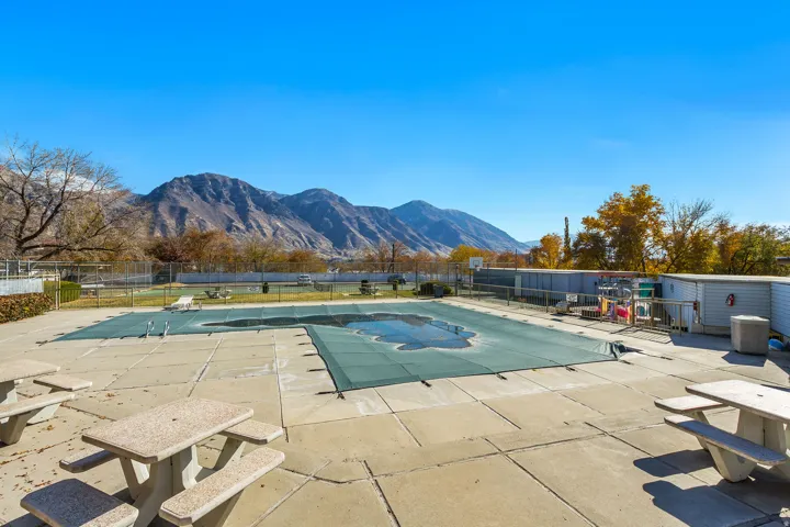 Community swimming pool with a covered pool deck, surrounding concrete patio, and picnic tables