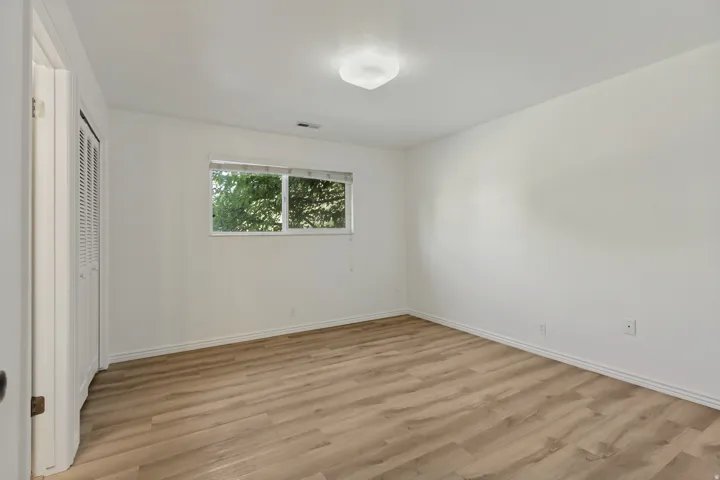 Wood-finish flooring with white trim, a double window, and a built-in closet with louvered doors