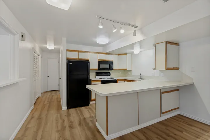Kitchen featuring L-shaped countertops, ample cabinetry, black appliances, and wood-finish flooring