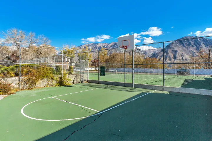 Outdoor court area featuring a basketball hoop and a fenced tennis court