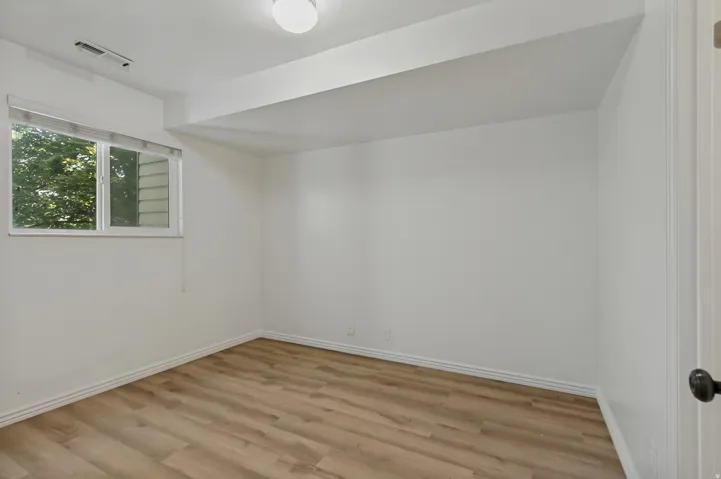 Wood-finish flooring, white walls, and a window with exterior tree scenery