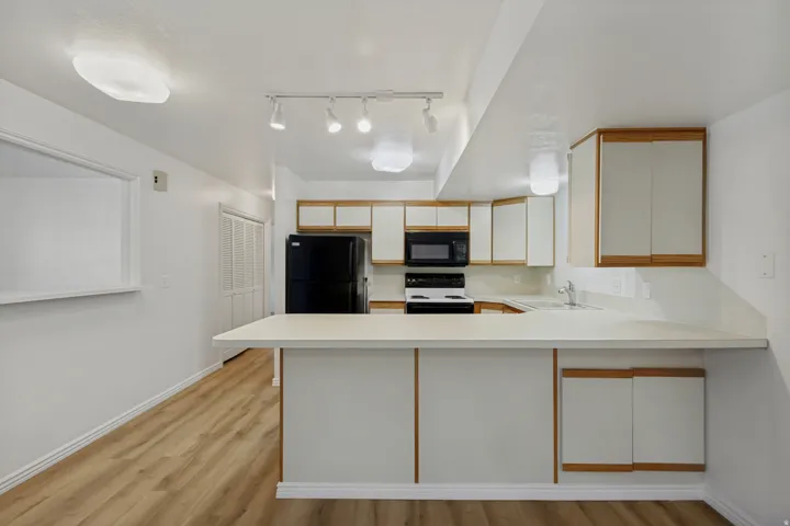 Modern kitchen featuring white cabinetry with wood-finish trim, stainless steel appliances, a waterfall-edge countertop with undermount sink, pendant lighting, and wood-finish flooring throughout the open layout