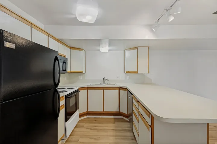 Kitchen featuring a U-shaped countertop, wood-finish flooring, white cabinetry with wood trim, and a full suite of black appliances