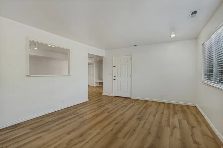 Wood-finish flooring, white walls, recessed ceiling lighting, a window with blinds, and an interior pass-through
