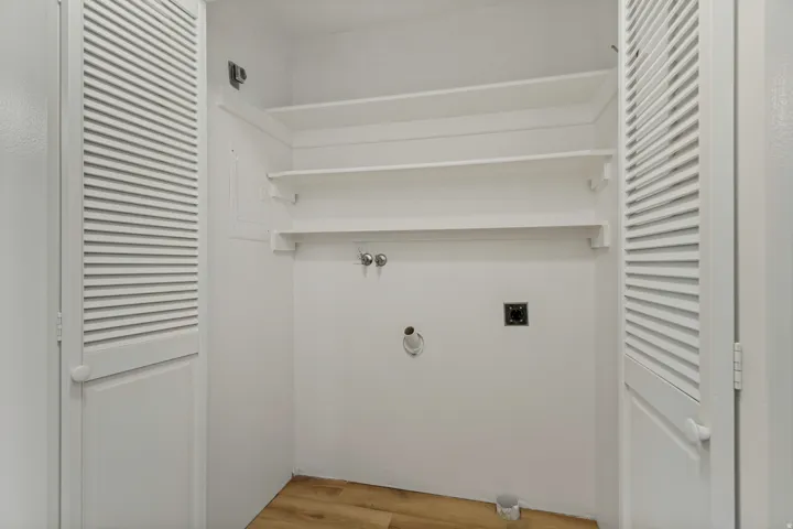 Laundry area with wood-finish flooring, louvered bi-fold doors, and built-in shelving