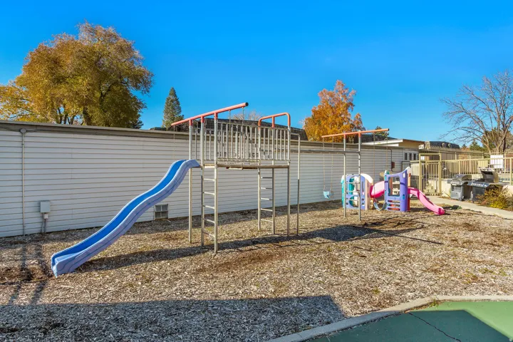 Recreational area featuring a playground structure with a blue slide, a secondary play structure, and wood chip ground cover