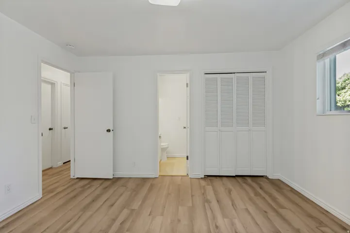 Wood-finish flooring, white walls, louvered bi-fold closet doors, and white trim