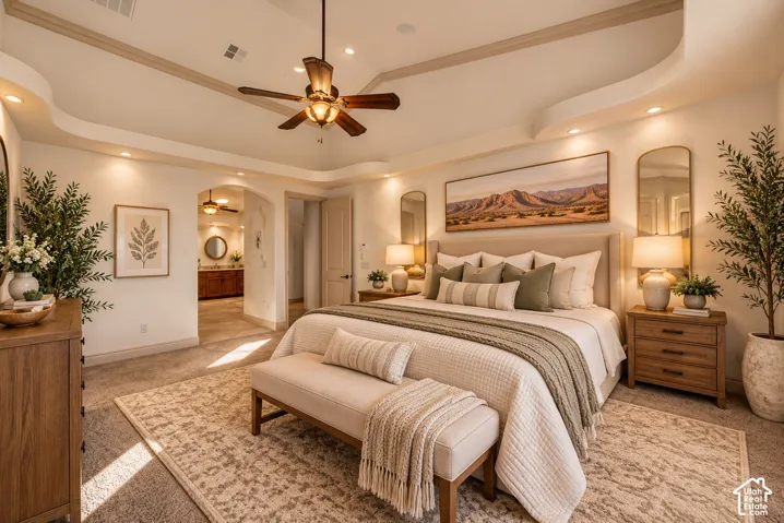 Tray ceiling with recessed lighting, ceiling fan, carpet flooring, and an arched doorway leading to an additional space with a built-in vanity
