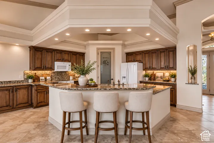 Kitchen featuring extensive wood cabinetry, stone countertops, a multi-level ceiling with recessed lighting, tile flooring, and a central island with bar seating