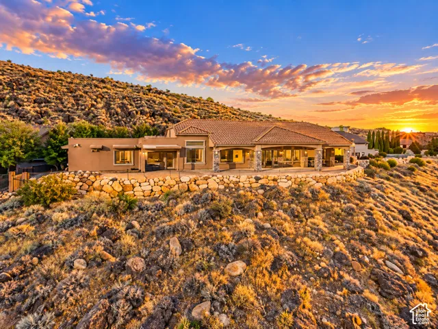 Terracotta tile roof, stucco exterior, expansive patio, stone retaining wall, and integrated exterior lighting