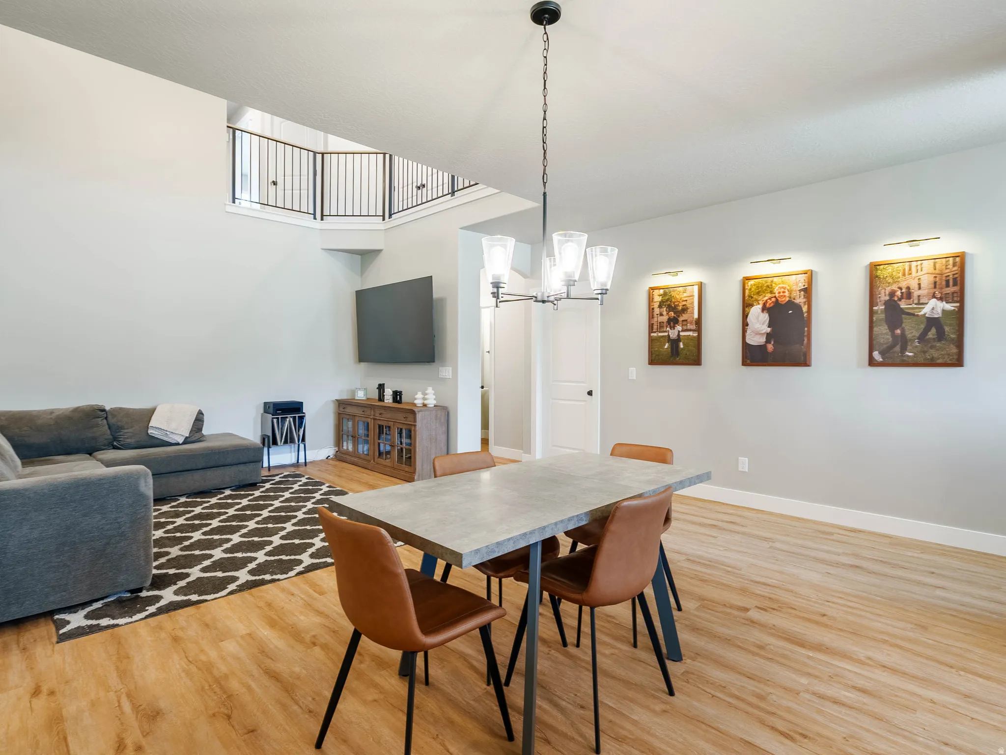Open-concept living area featuring wood-finish flooring, a two-story ceiling, and a prominent dining space with an overhead chandelier