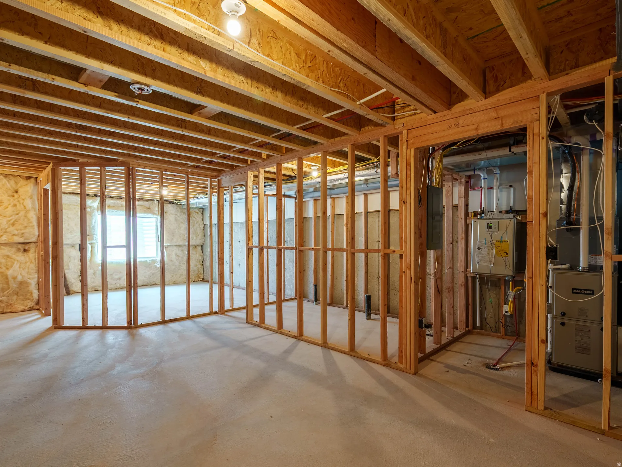 Unfinished basement space featuring exposed wooden framing, an existing furnace system, and visible insulation