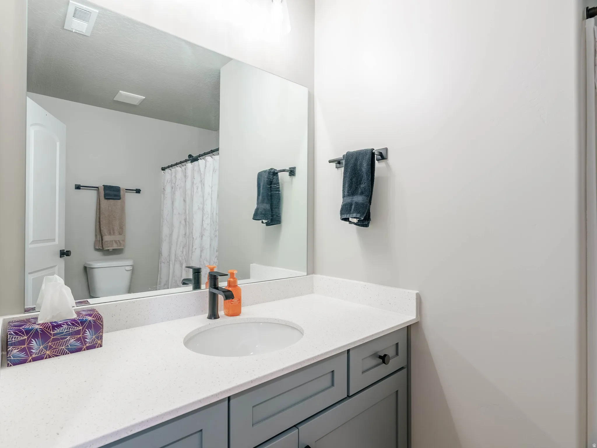 Bathroom vanity featuring a light-toned countertop, undermount sink, and matte black faucet