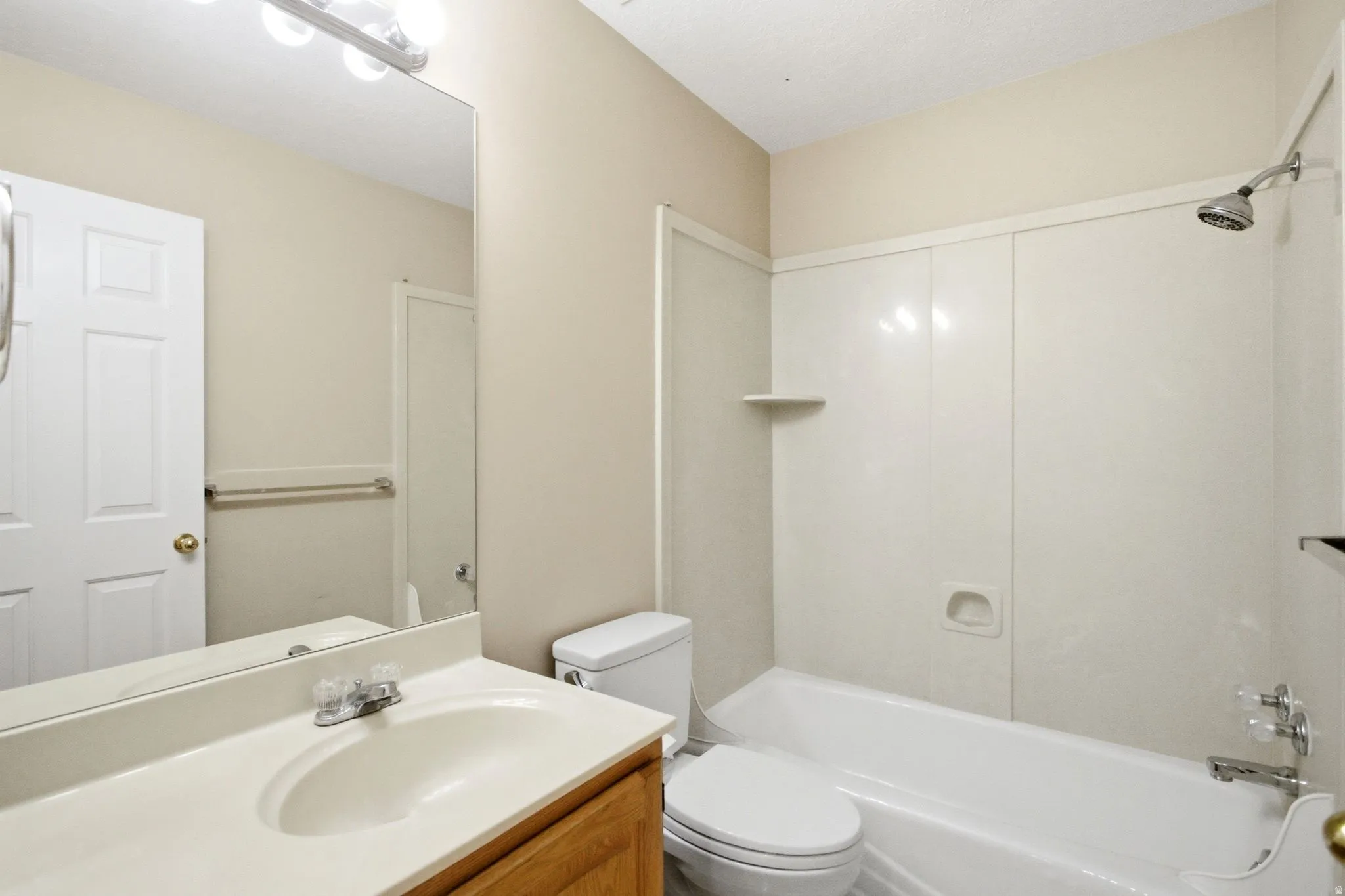 Bathroom featuring a vanity with an integrated sink, a large wall-mounted mirror, a three-light fixture, a bathtub with a shower combination, and a toilet