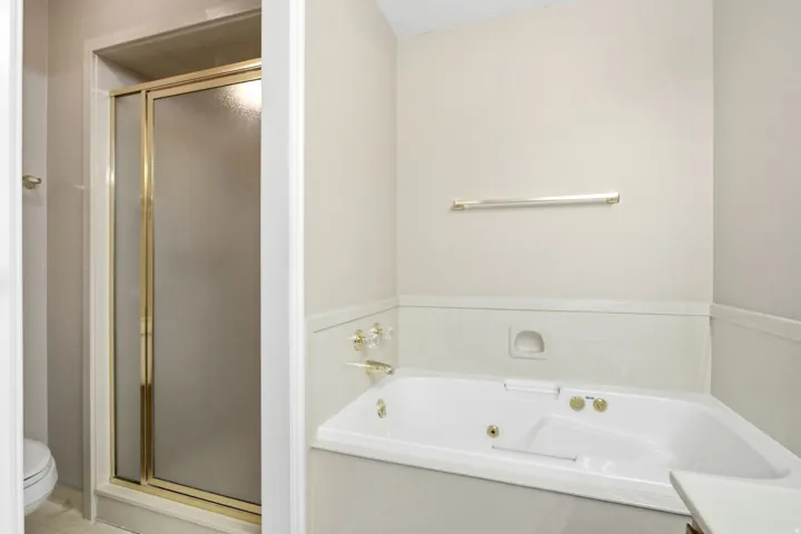 Bathroom featuring an enclosed shower with gold-tone framing and a built-in corner tub with gold-tone fixtures