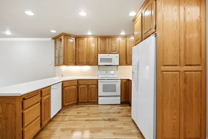 Open kitchen featuring wood-finish flooring, white countertops, recessed lighting, and ample wood cabinetry including a pantry