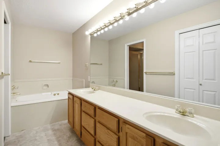 Bathroom featuring a dual vanity with light wood cabinetry, a large wall-mounted mirror, and a built-in bathtub with gold-tone fixtures