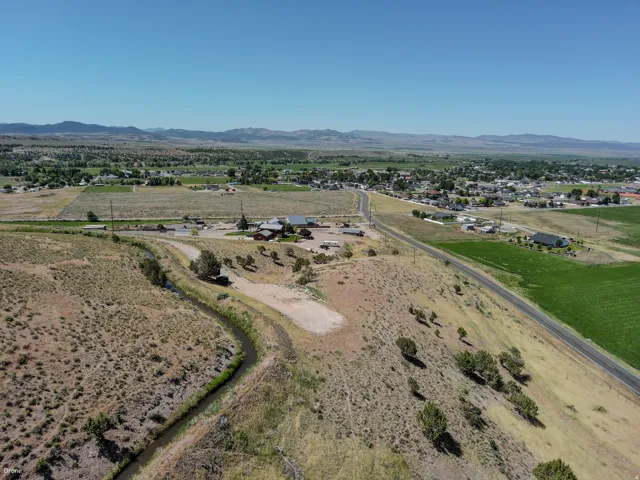 Expansive rural landscape featuring a winding irrigation canal, a paved road, scattered trees, and distant mountainous terrain under a clear sky