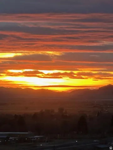 Expansive mountain range backdrop with a dramatic sunset, showcasing vibrant orange, red, and yellow hues across the sky