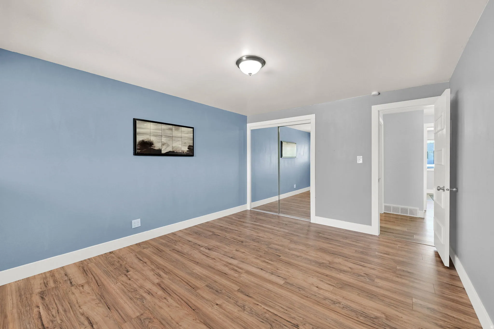 Spacious room featuring wood-finish flooring, a ceiling-mounted light fixture, and white trim
