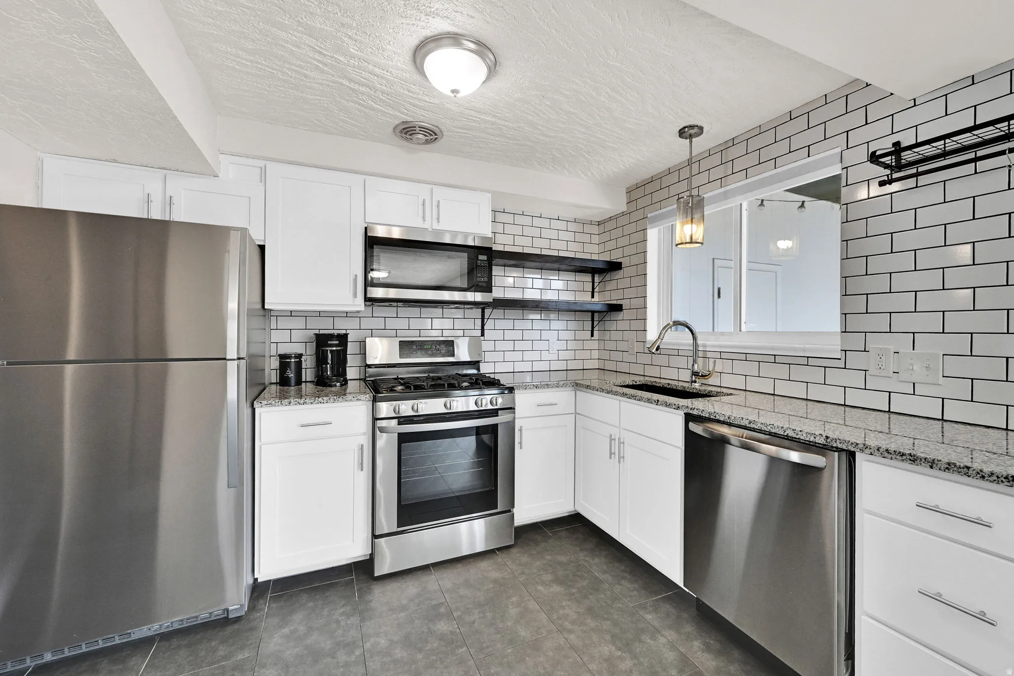 Modern kitchen featuring stainless steel appliances, white subway tile backsplash, white cabinetry with contemporary hardware, stone-finish countertops, and dark tile flooring