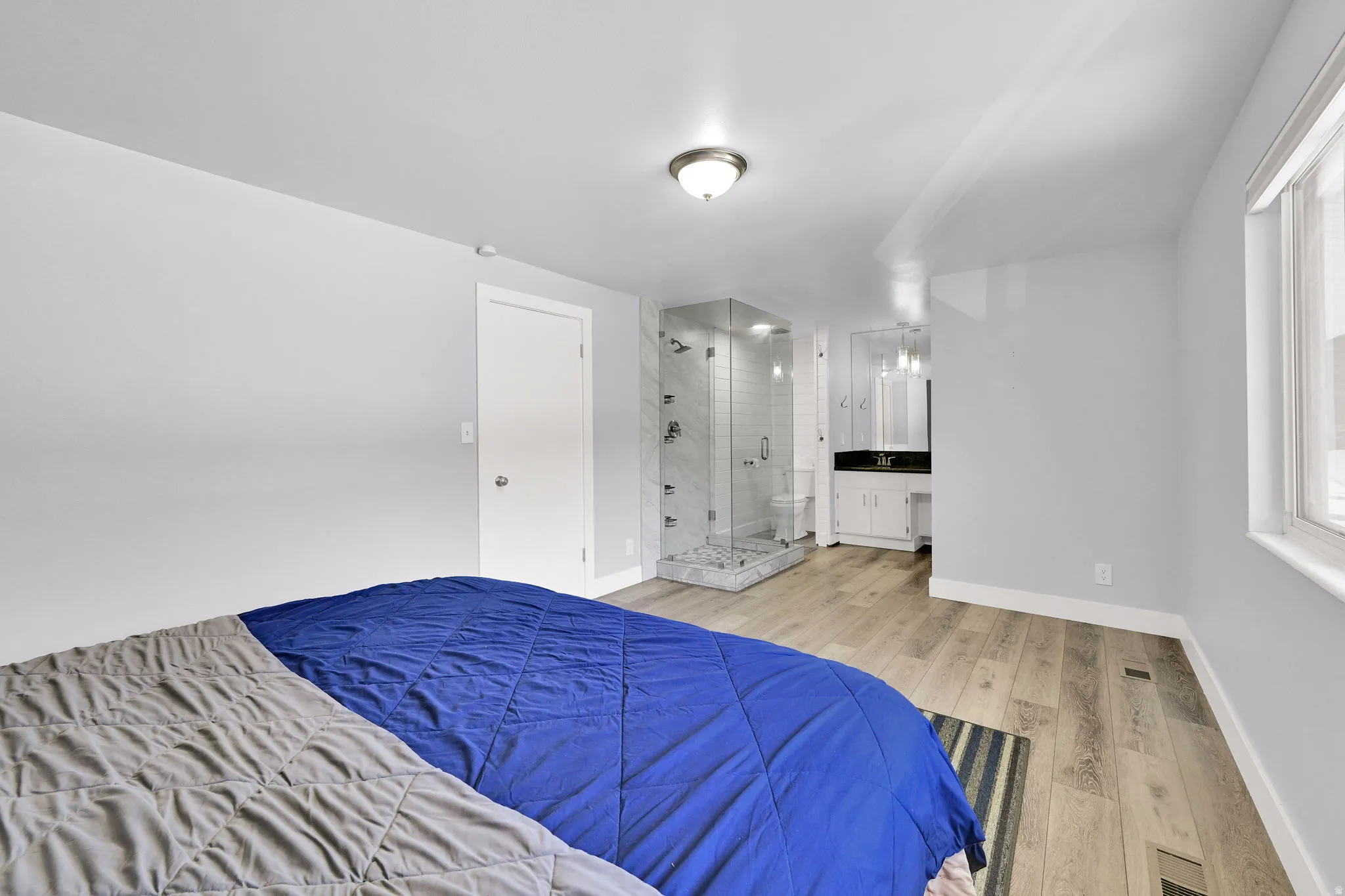Spacious room featuring wood-finish flooring, a large window, and a glass-enclosed shower with tile surround