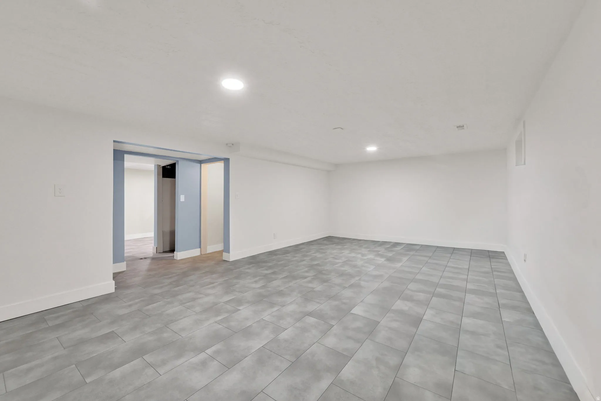 Spacious room featuring light gray tile flooring, white walls, and recessed lighting