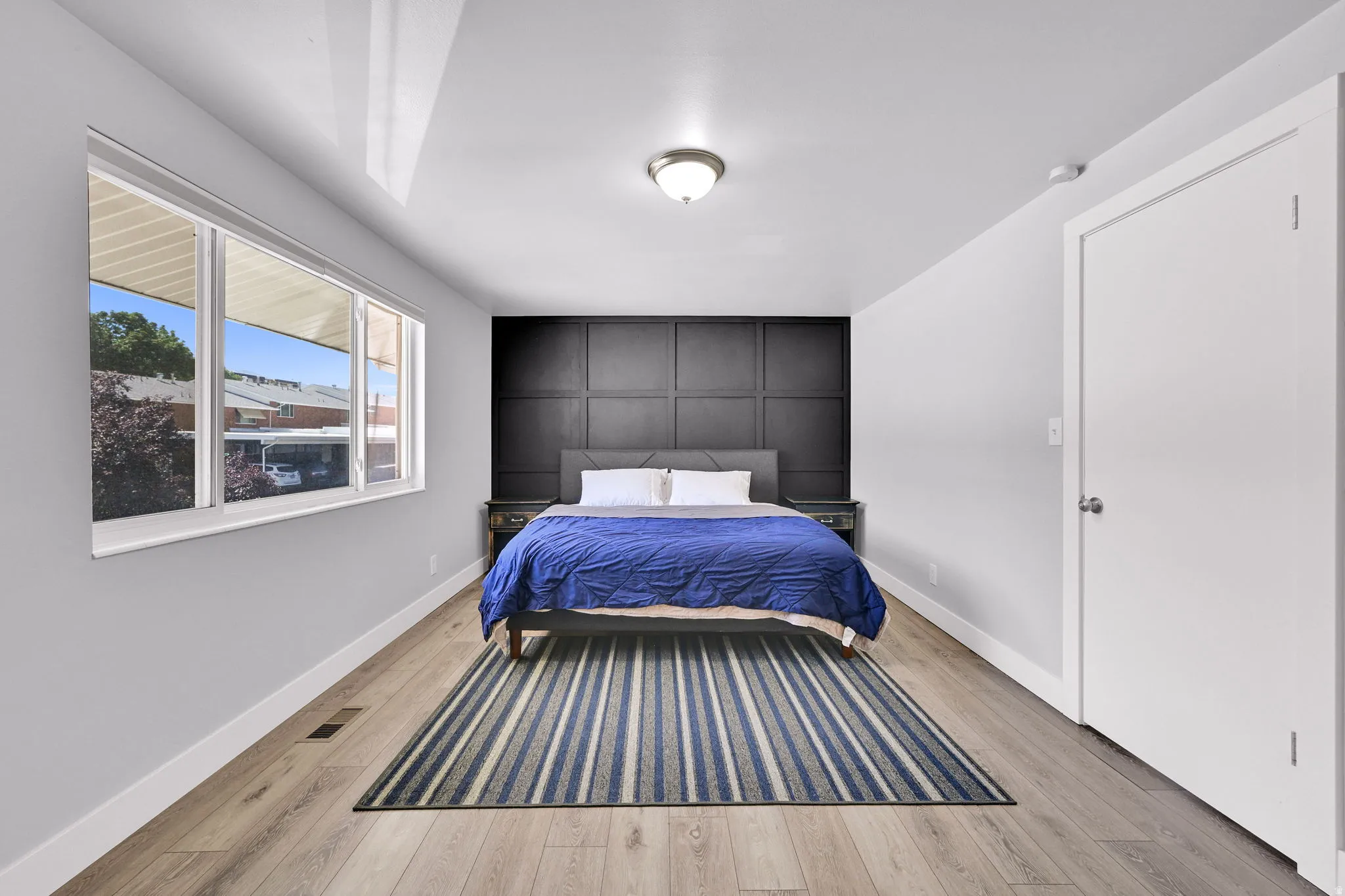 Bedroom featuring a paneled accent wall, wood-finish flooring, and white trim