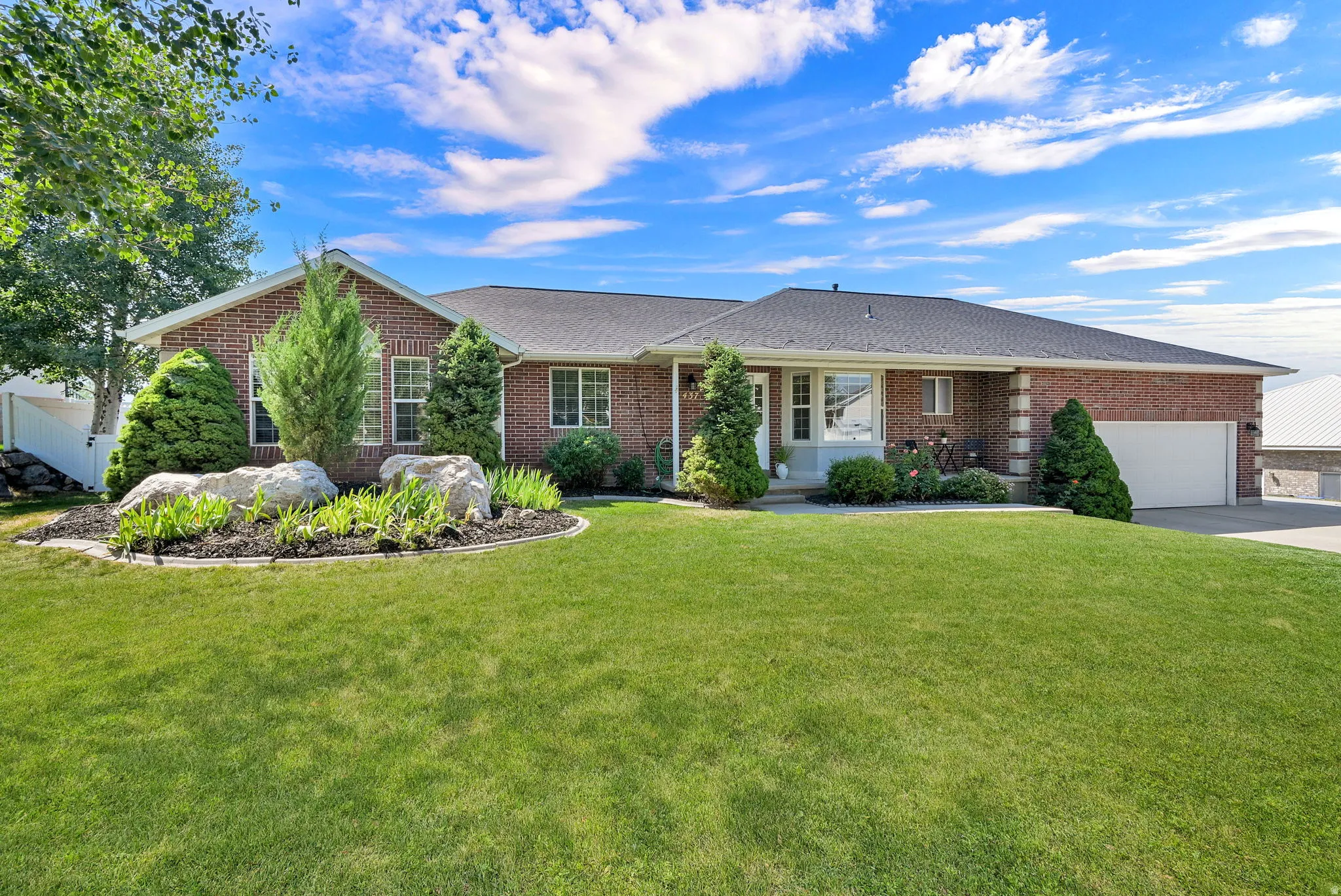Brick exterior residence featuring a two-car garage, established front yard landscaping, and a white picket fence on the side