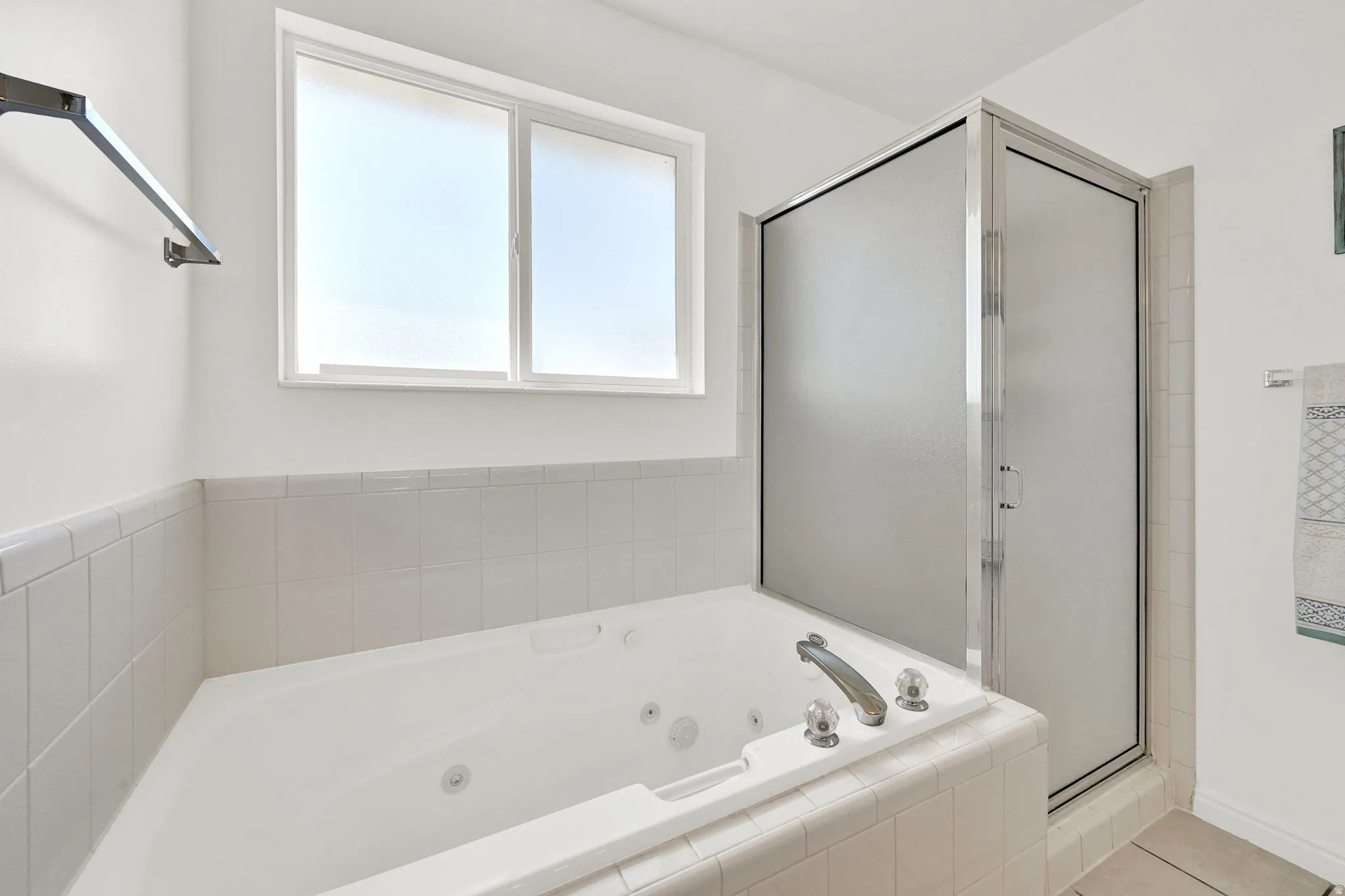 Built-in jetted tub with chrome fixtures, surrounded by white tile and a privacy window