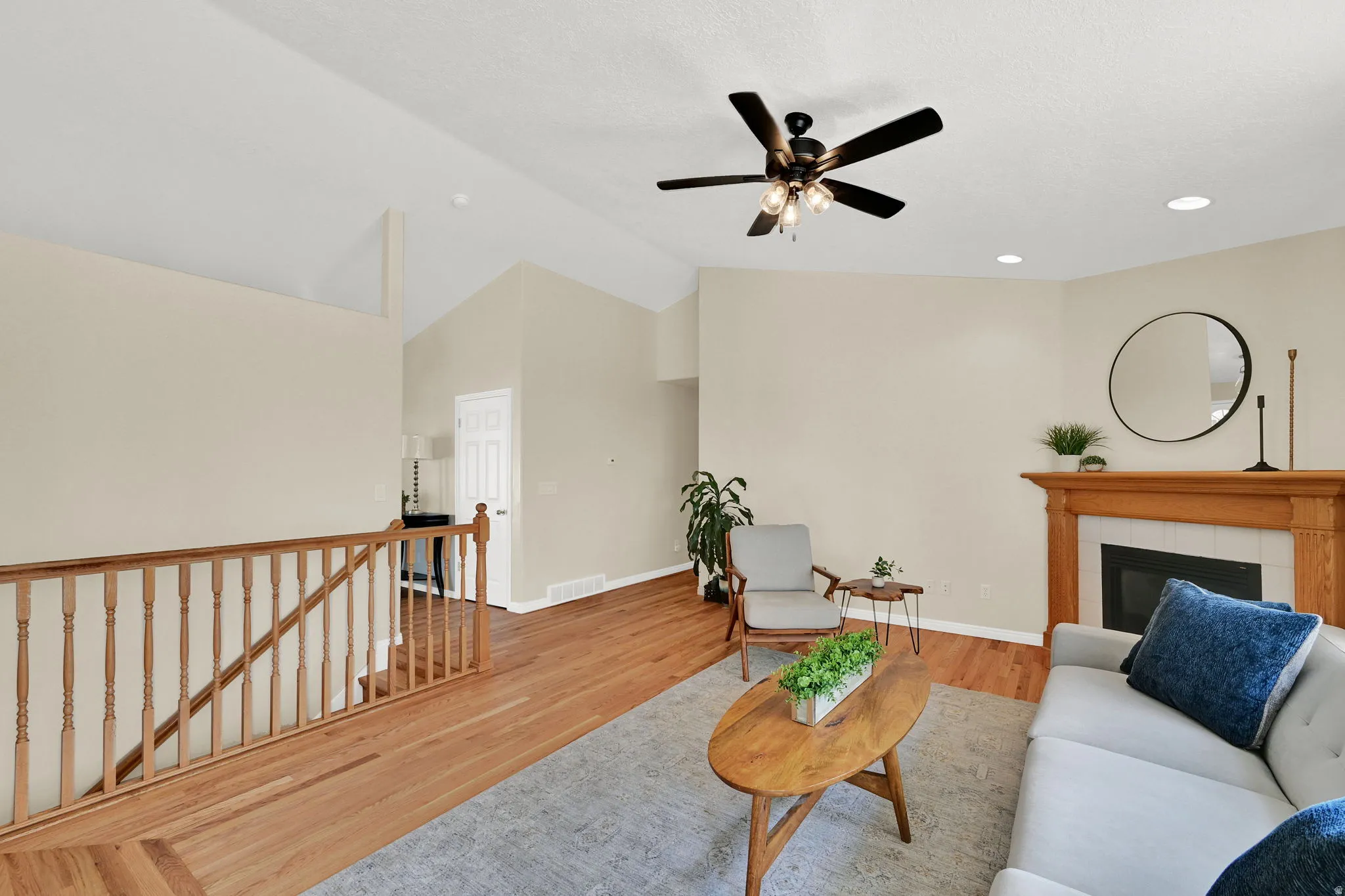 Spacious living area featuring vaulted ceilings, wood-finish flooring, a ceiling fan, and a fireplace with a wood mantel and tile surround
