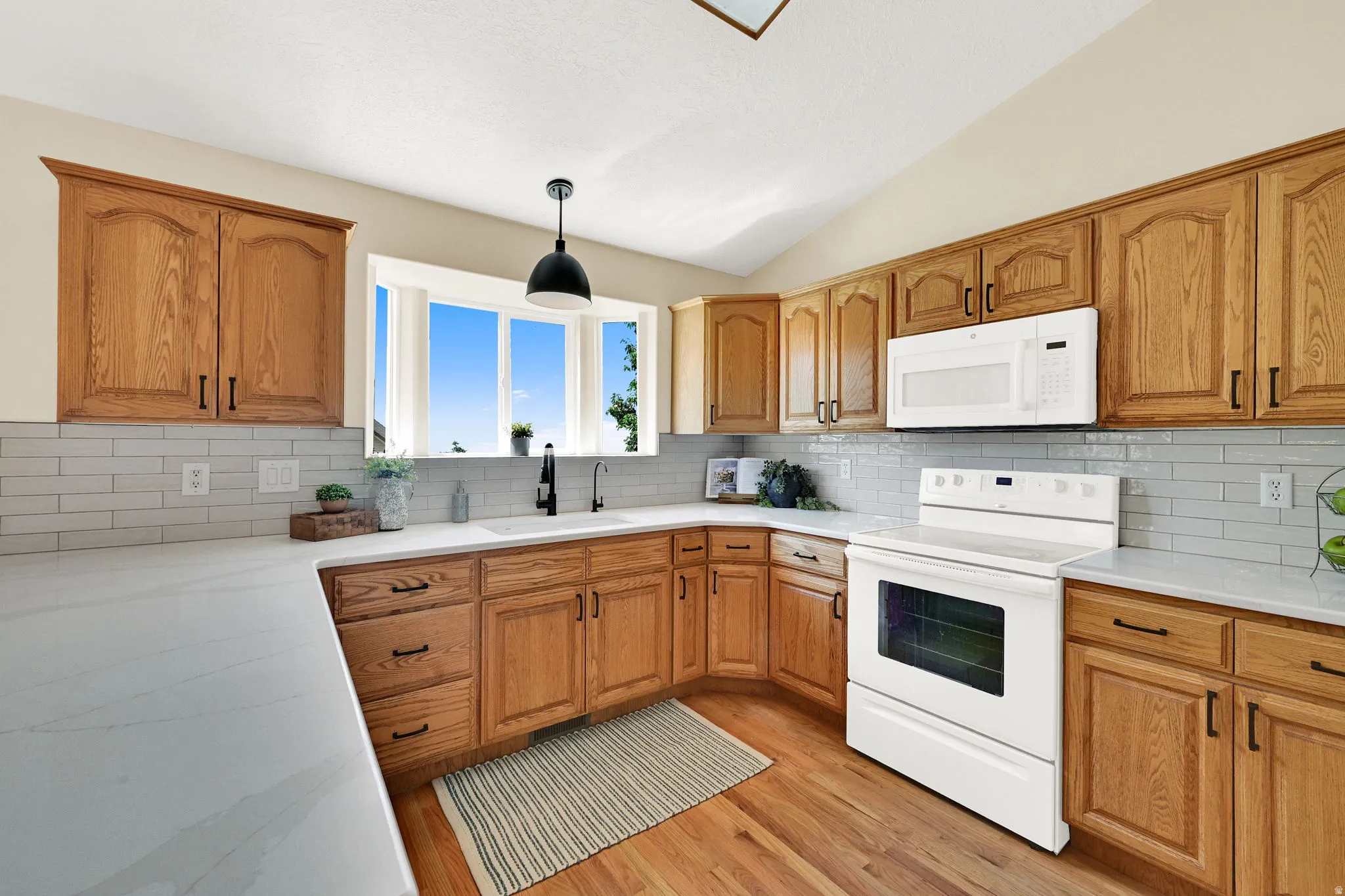 Expansive kitchen featuring wood-finish cabinetry, white countertops, subway tile backsplash, a bay window, and hardwood flooring