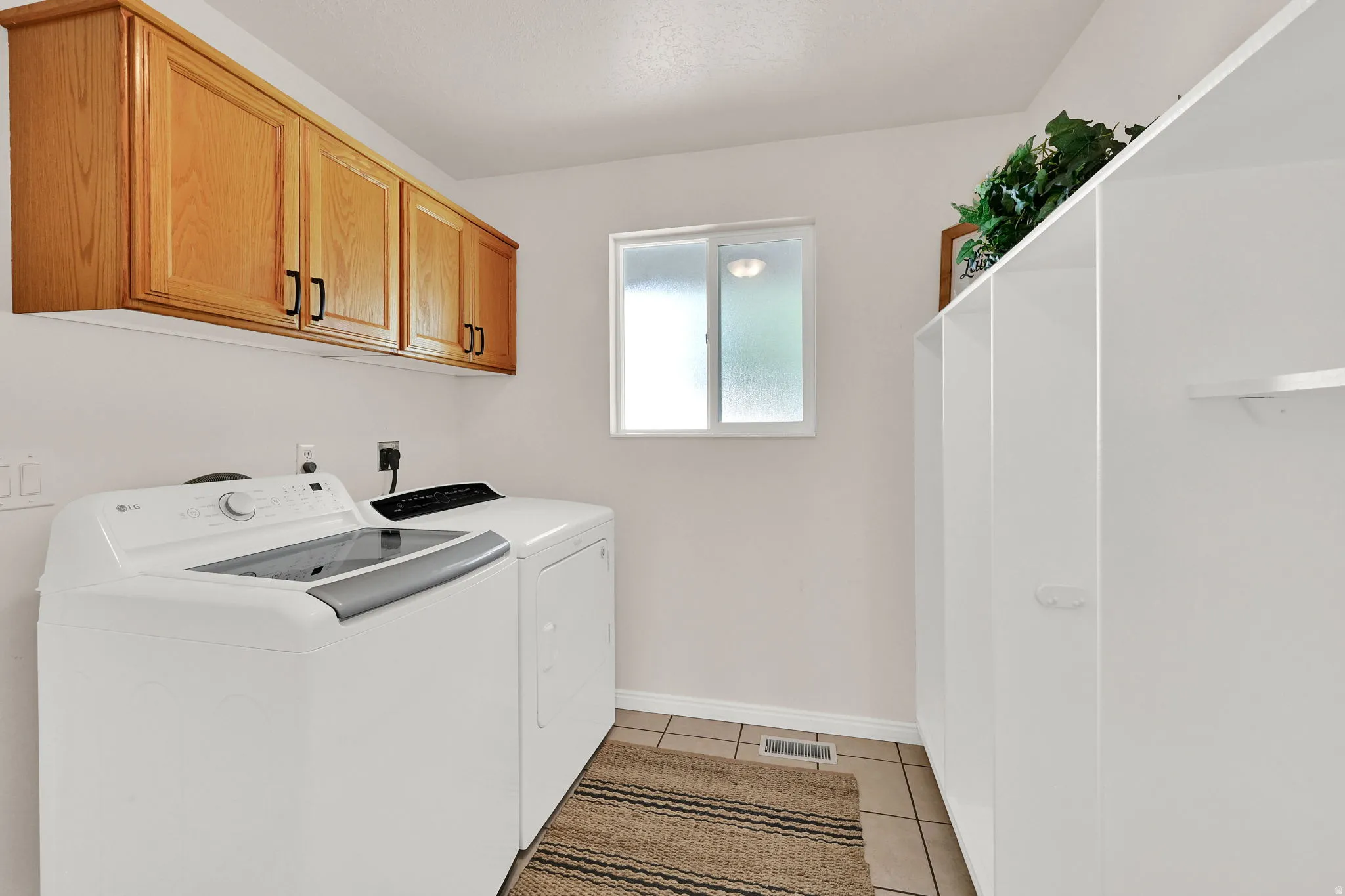 Utility room featuring overhead wood cabinetry, a window with frosted glass, tiled flooring, and built-in shelving